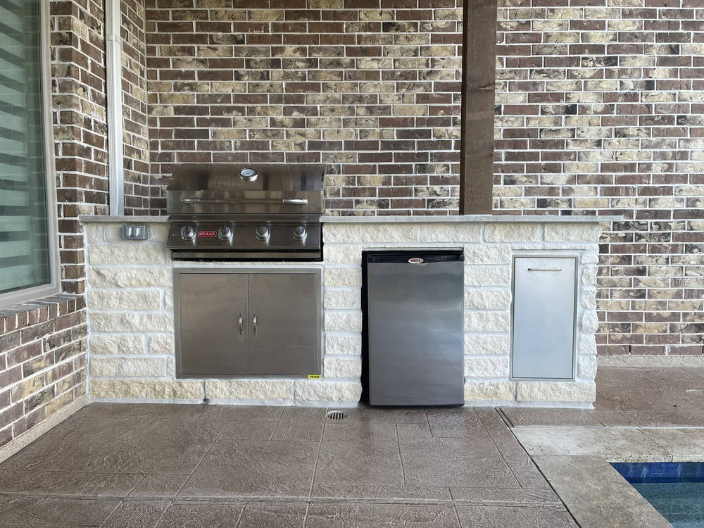 Stone outdoor kitchen with built-in grill and bar seating in Katy, TX